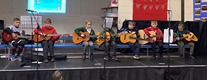 6 children on a stage playing the guitar